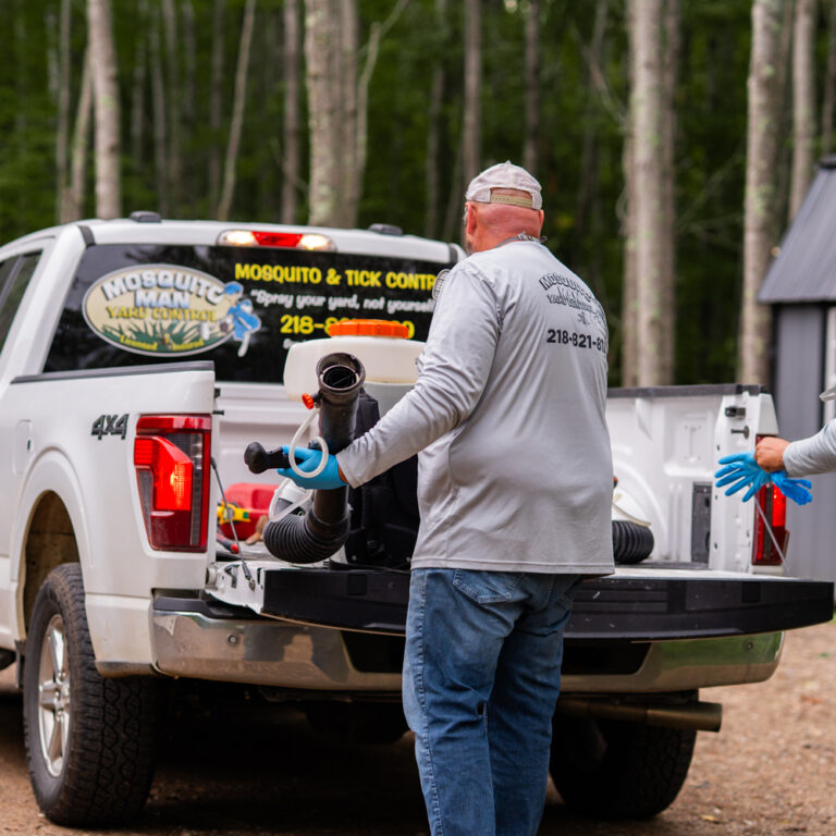 Two Mosquito Man technicians loading foggers and supplies from a work truck.